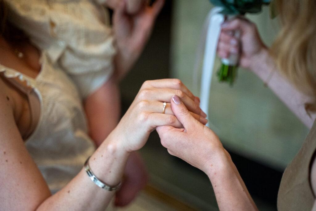 Handen van het bruidspaar met trouwring tijdens een intiem moment, vastgelegd in natuurlijke bruiloft fotografie.