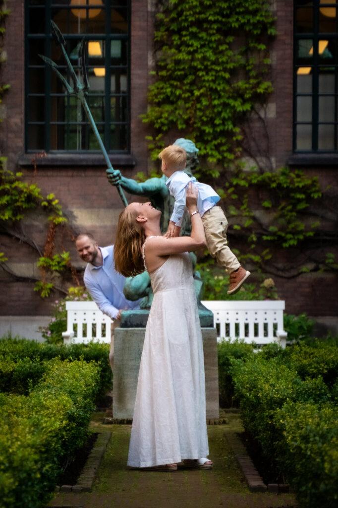 Moeder tilt haar kind omhoog in een tuin tijdens de bruiloft, speels en liefdevol vastgelegd.
