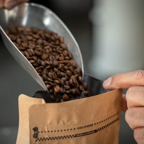 Vers gebrande koffiebonen worden met een schep in een kraft zak gedaan bij Lorando & Morini.
