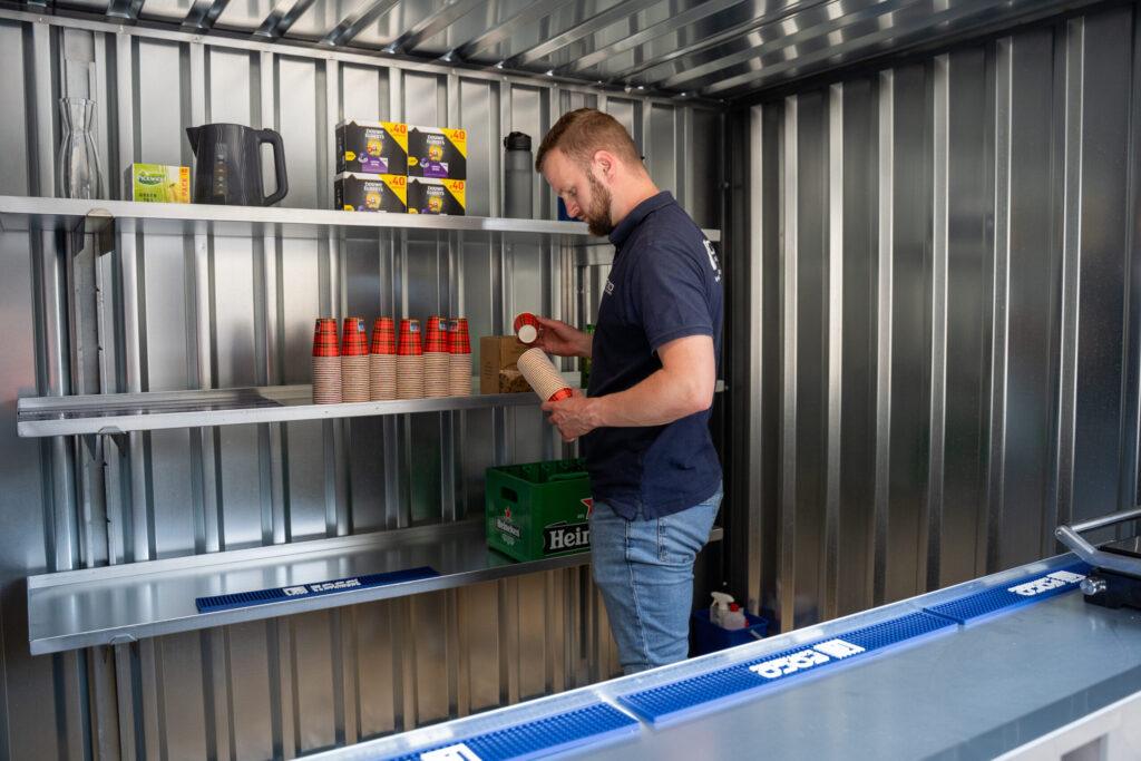 Foldaco-medewerker vult bekers en voorraad aan in een metalen container.
