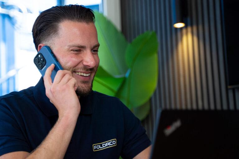 Medewerker van Foldaco voert een telefoongesprek terwijl hij achter een laptop zit.