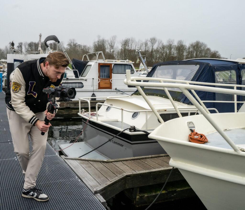 “Videograaf filmt met een gimbal camera vanaf de steiger in een jachthaven met witte boten op de achtergrond.”