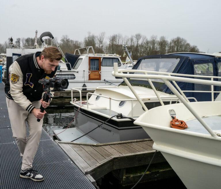 “Videograaf filmt met een gimbal camera vanaf de steiger in een jachthaven met witte boten op de achtergrond.”