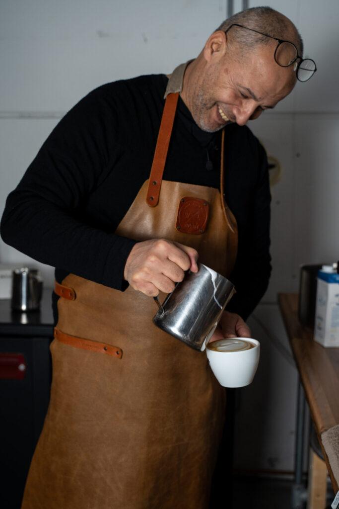 Koffiebrander schenkt melk in een cappuccino met latte art bij Lorando & Morini.