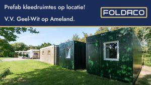 Twee donkergroene Foldaco prefab kleedruimtes op een grasveld naast een sportcomplex van V.V. Geel-Wit op Ameland, met bomen en een gebouw op de achtergrond.