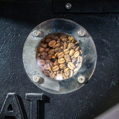 Vers gebrande koffiebonen zichtbaar door het kijkvenster van de koffiebrander bij Lorando & Morini.
