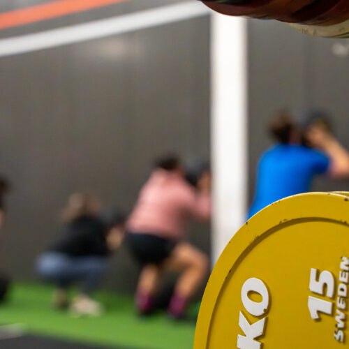 Halterschijf in CrossFit Gold Pact gym met sporters die op de achtergrond trainen