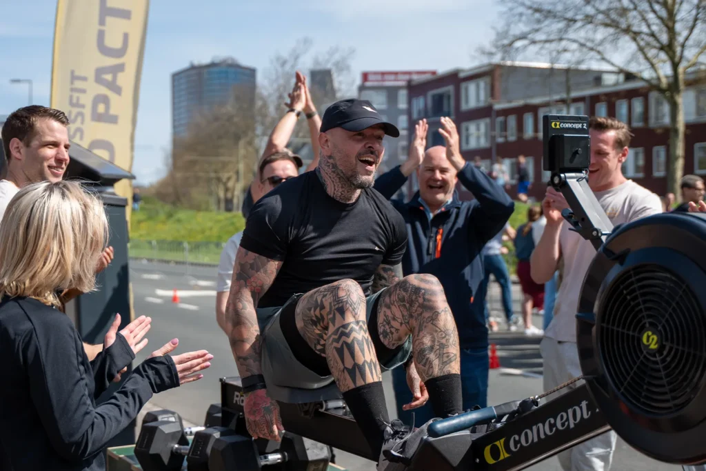 Man op roeimachine wordt aangemoedigd door publiek tijdens marathon evenement.