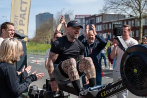 Man op roeimachine wordt aangemoedigd door publiek tijdens marathon evenement.