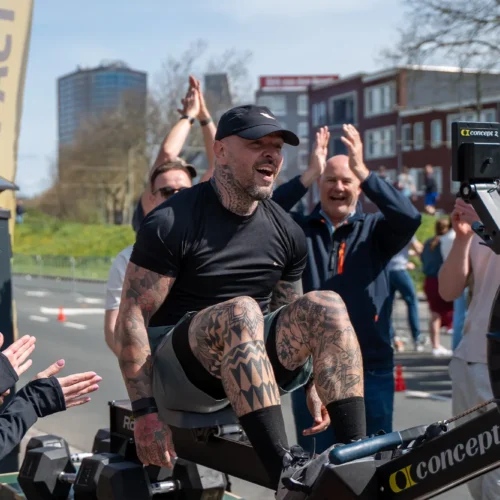 Man op roeimachine wordt aangemoedigd door publiek tijdens marathon evenement.