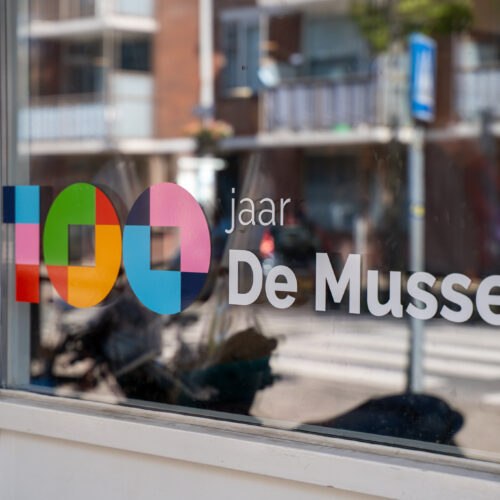 100 jaar jubileumlogo van De Mussen op een raam van het buurtcentrum.
