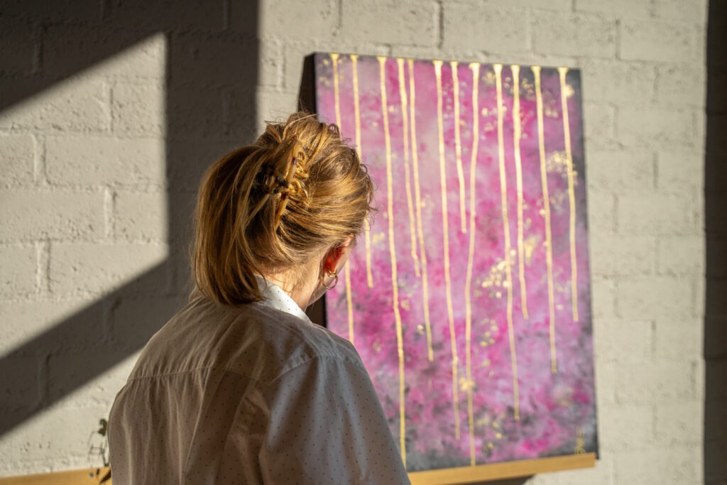 Bezoeker bekijkt een roze abstract schilderij met gouden details in het atelier van Studio Isobel.