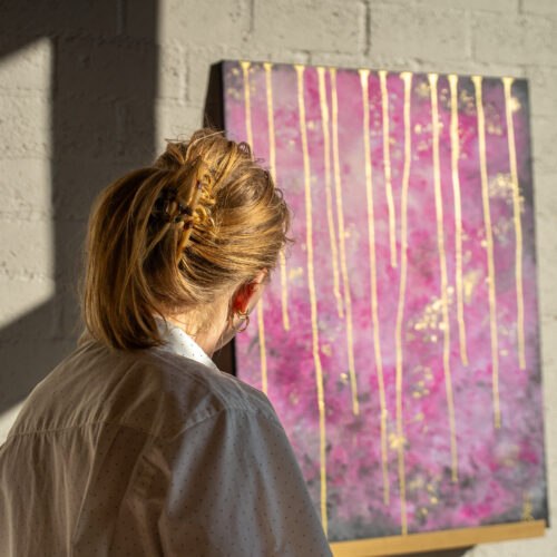 Bezoeker bekijkt een roze abstract schilderij met gouden details in het atelier van Studio Isobel.