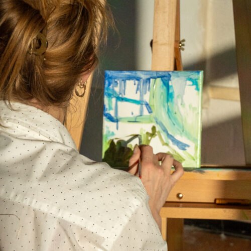 Kunstenaar van Studio Isobel werkt aan een nieuw schilderij op een ezel in warm natuurlijk licht.