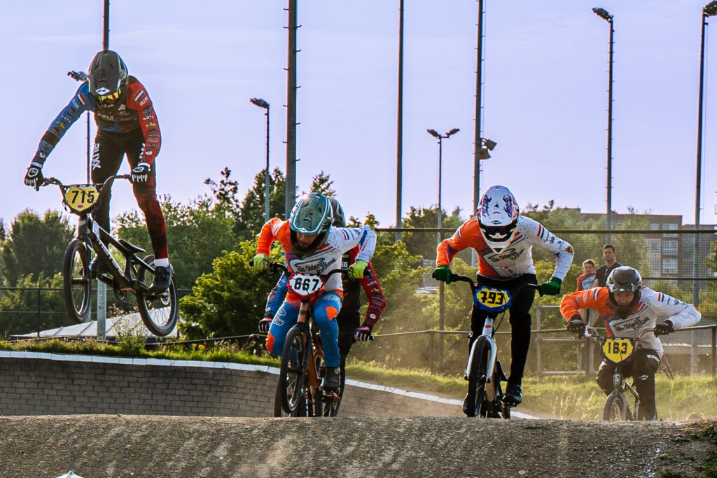 Meerdere BMX-rijders springen tegelijk over een heuvel tijdens de wedstrijd.