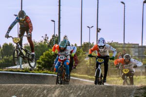 Meerdere BMX-rijders springen tegelijk over een heuvel tijdens de wedstrijd.
