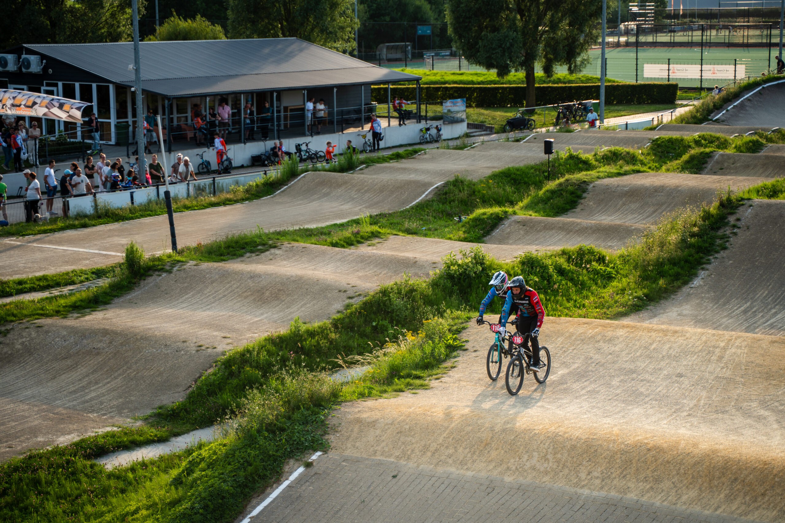 Overzichtsfoto van de BMX-baan met twee rijders en publiek langs de kant.