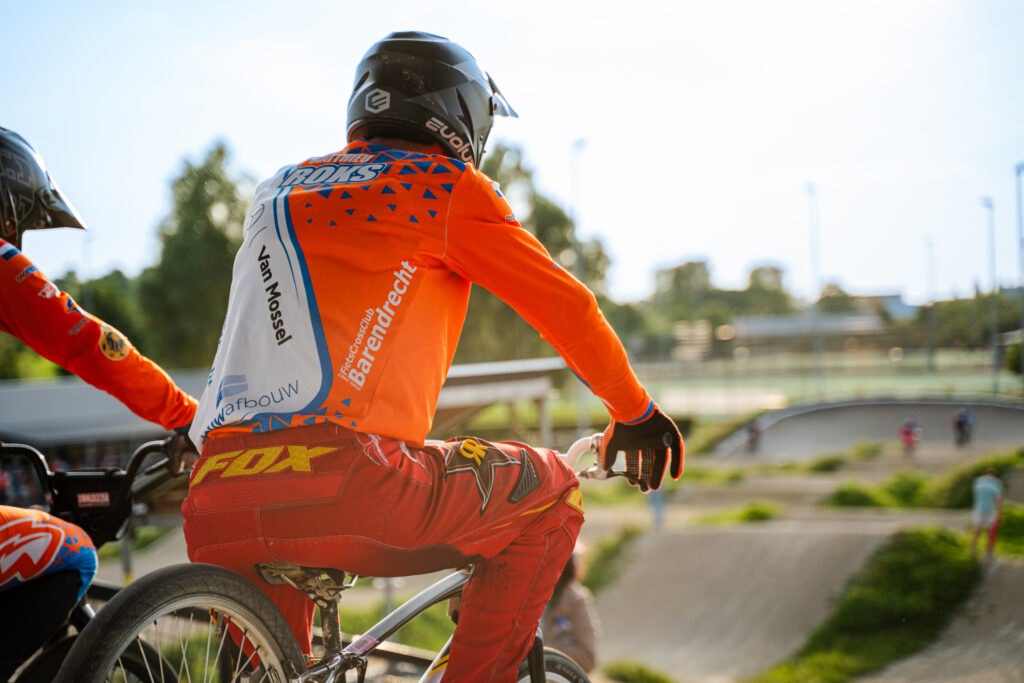 BMX-rijder wacht bovenaan het starthek en kijkt uit over de baan.