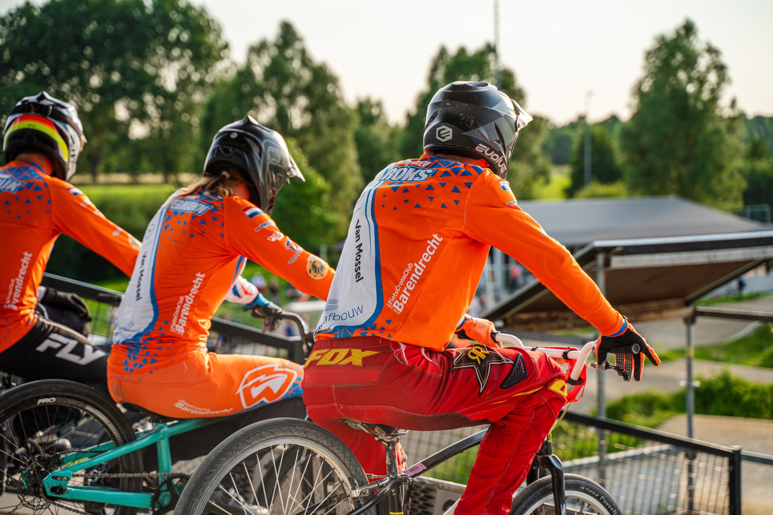Meerdere BMX-rijders wachten bovenaan het starthek bij zonsondergang.