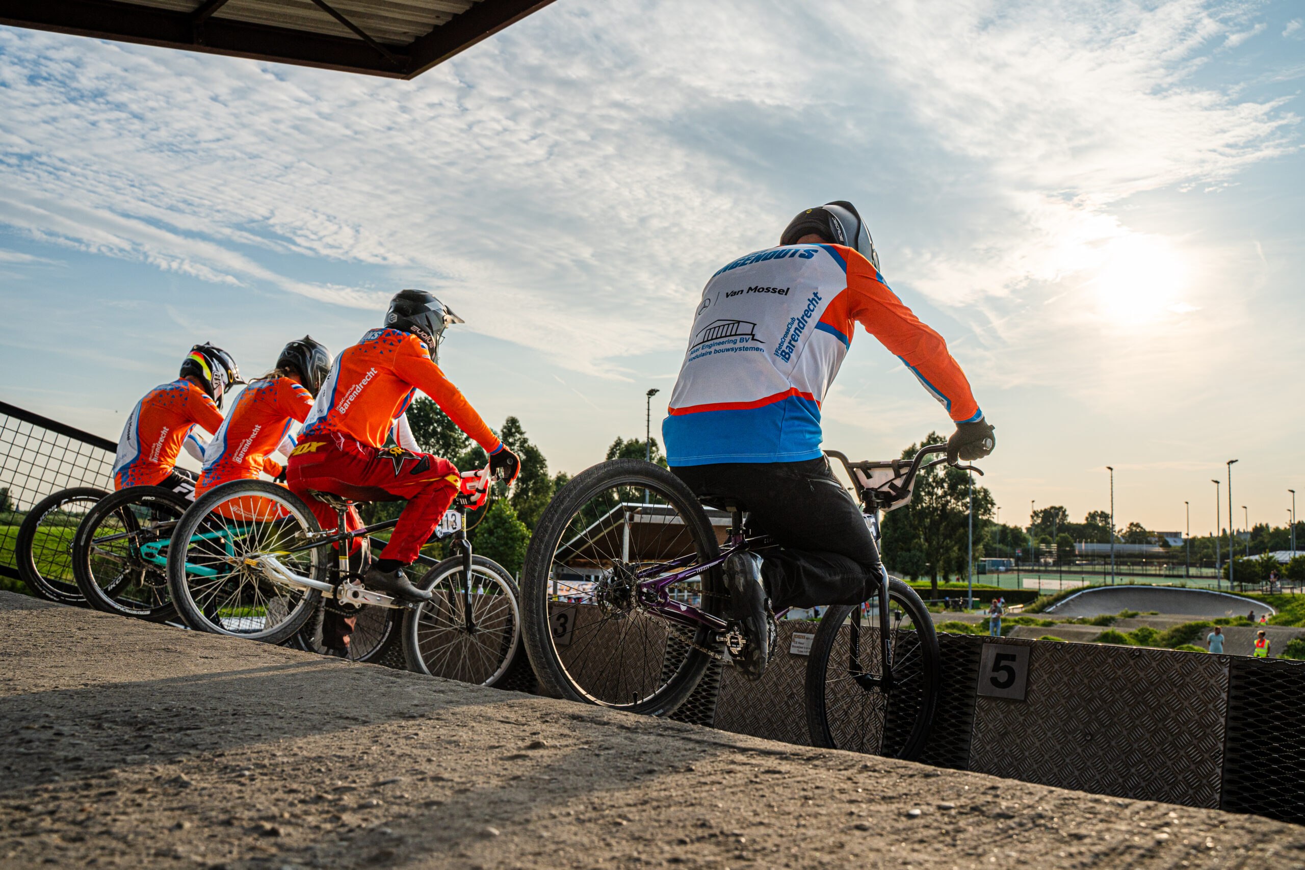 Meerdere BMX-rijders staan klaar bovenaan het starthek met uitzicht over de baan.